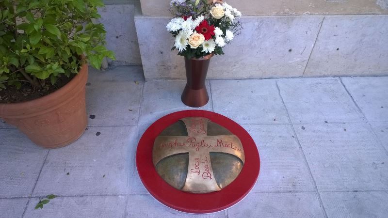 Medaglione in bronzo collocato vicino l'ingresso della Casa-Museo dove visse il Beato Puglisi. Il medaglione indica il punto in cui venne ucciso. Realizzato da Grazia Pernice, volontaria del Centro di Accoglienza Padre Nostro